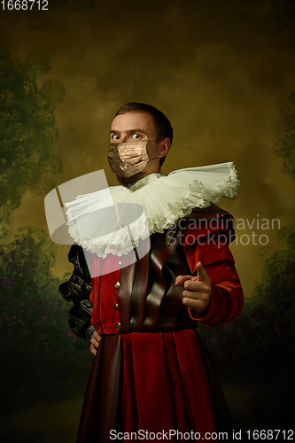 Image of Portrait of medieval young man in vintage clothing and golden face mask standing on dark background.