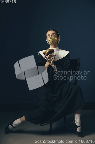 Image of Medieval young woman as a nun in vintage clothing and golden face mask on dark blue background. Concept of comparison of eras, protection from covid