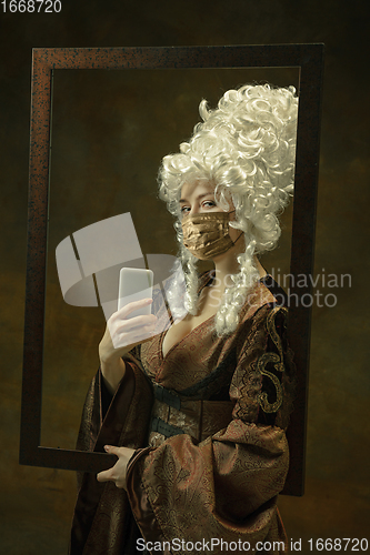 Image of Portrait of medieval young woman in vintage clothes and golden face mask on dark background.