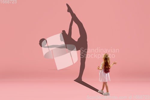 Image of Childhood and dream about big and famous future. Conceptual image with girl and shadow of fit female rhythm gymnast on coral pink background