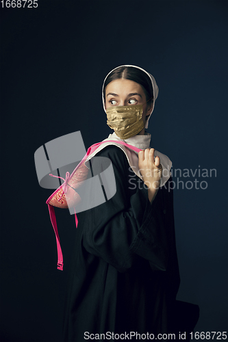 Image of Medieval young woman as a nun in vintage clothing and golden face mask on dark blue background. Concept of comparison of eras, protection from covid