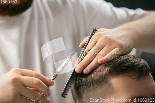 Image of Close up hands of master barber, stylist does the hairstyle to guy, young man. Professional occupation, male beauty concept