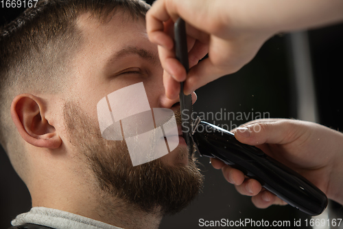 Image of Close up of client of master barber, stylist during getting care of mustache and beard. Professional occupation, male beauty concept