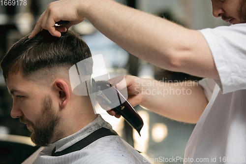 Image of Close up master barber, stylist does the hairstyle to guy, young man. Professional occupation, male beauty concept