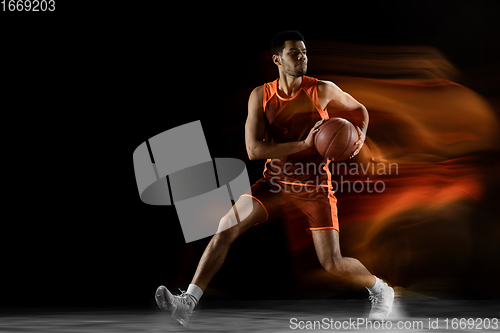 Image of Young arabian basketball player of team in action, motion isolated on black background in mixed light. Concept of sport, movement, energy and dynamic.
