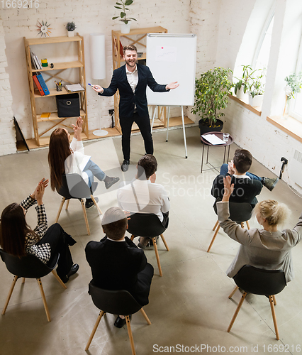 Image of Male speaker giving presentation in hall at workshop. Audience or conference hall. High angle of unrecognized participants.