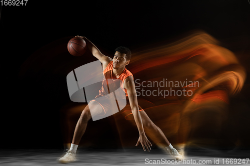 Image of Young arabian basketball player of team in action, motion isolated on black background in mixed light. Concept of sport, movement, energy and dynamic.