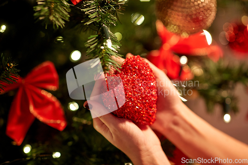 Image of hands decorating christmas tree with red heart