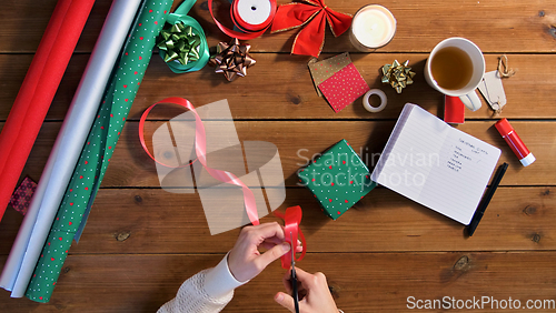 Image of hands packing christmas gift and cutting ribbon