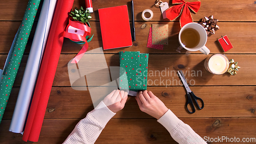 Image of hands wrapping christmas gift into paper at home