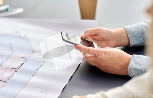 Image of hands with smartphone and blueprint at office