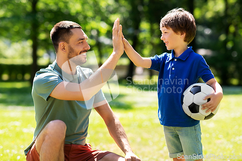 Image of father giving five to son with soccer ball at park