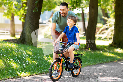 Image of father teaching little son to ride bicycle at park