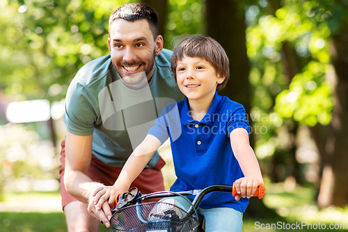 Image of father teaching little son to ride bicycle at park