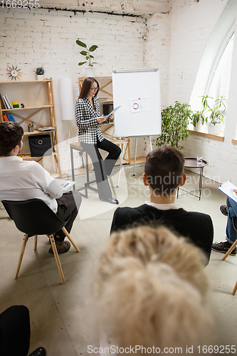 Image of Female speaker giving presentation in hall at workshop. Audience or conference hall. Rear rview of unrecognized participants.