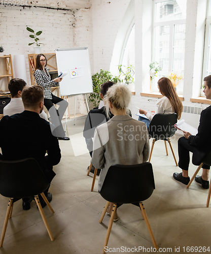 Image of Female speaker giving presentation in hall at workshop. Audience or conference hall. Rear view of unrecognized participants.