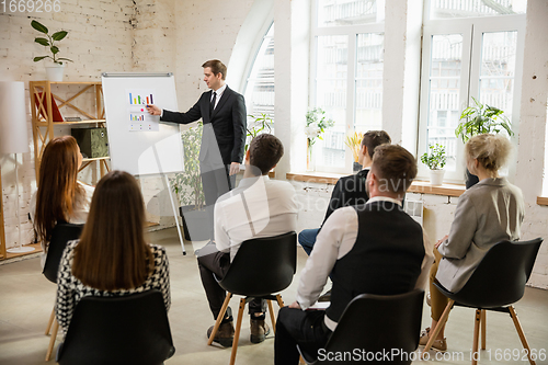 Image of Male speaker giving presentation in hall at workshop. Audience or conference hall. Rear view of unrecognized participants.