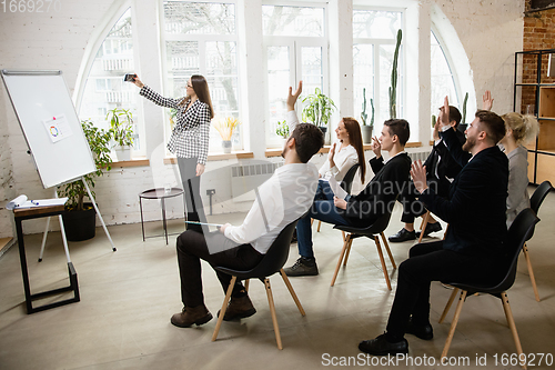 Image of Female speaker giving presentation in hall at workshop. Audience or conference hall. Side view of unrecognized participants.