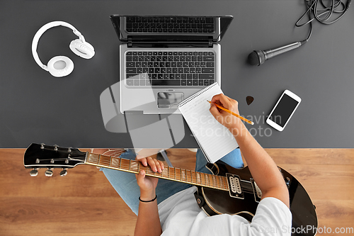 Image of man with guitar writing to music book at table