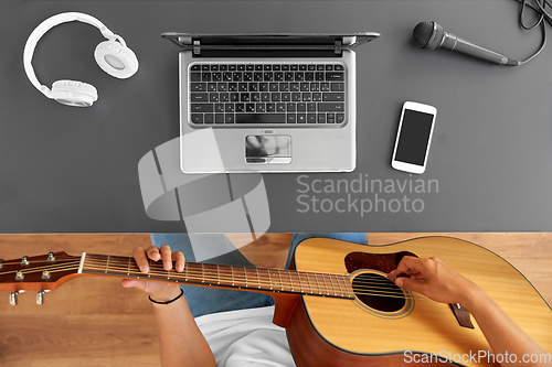 Image of young man with laptop playing guitar at table