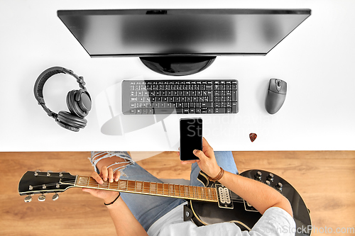 Image of young man with guitar and smartphone at table