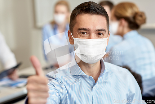 Image of businessman in mask showing thumbs up at office
