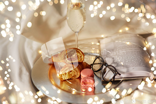 Image of champagne, croissants, book and glasses in bed