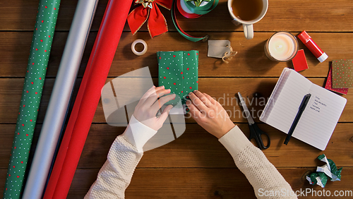 Image of hands wrapping christmas gift into paper at home