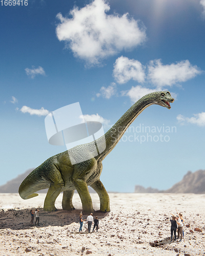 Image of Dinosaur huge higth walking through the sunny desert comes across little shocked group of people