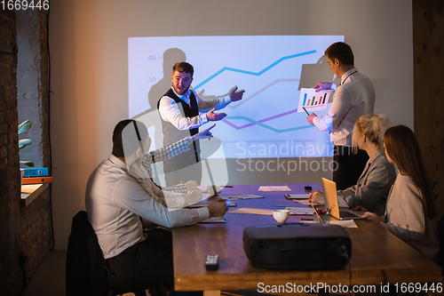 Image of Male speaker giving presentation in hall at workshop. Audience or conference hall. Participants, co-workers listening at the table.