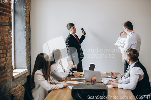 Image of Male speaker giving presentation in hall at workshop. Audience or conference hall. Participants, co-workers listening at the table.