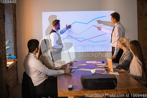 Image of Male speaker giving presentation in hall at workshop. Audience or conference hall. Participants, co-workers listening at the table.