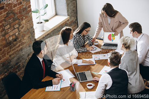 Image of Female speaker giving presentation in hall at workshop. Audience or conference hall. Participants, co-workers listening at the table.