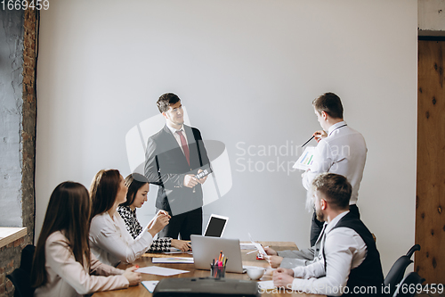 Image of Male speaker giving presentation in hall at workshop. Audience or conference hall. Participants, co-workers listening at the table.