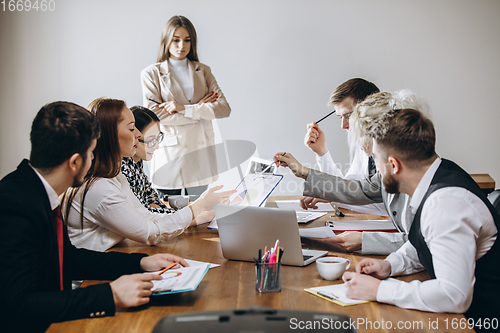 Image of Female speaker giving presentation in hall at workshop. Audience or conference hall. Participants, co-workers listening at the table.