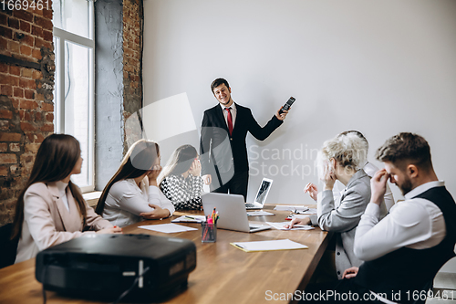 Image of Male speaker giving presentation in hall at workshop. Audience or conference hall. Participants, co-workers listening at the table.