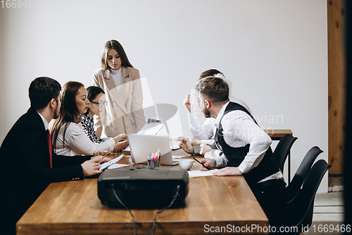 Image of Female speaker giving presentation in hall at workshop. Audience or conference hall. Participants, co-workers listening at the table.