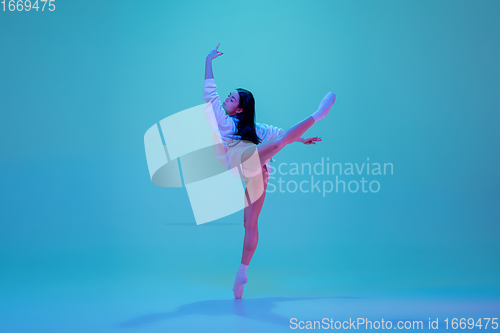 Image of Young and graceful ballet dancer isolated on blue studio background in neon light. Art, motion, action, flexibility, inspiration concept.