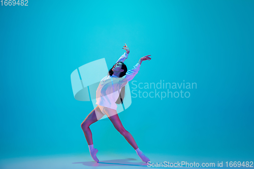 Image of Young and graceful ballet dancer isolated on blue studio background in neon light. Art, motion, action, flexibility, inspiration concept.