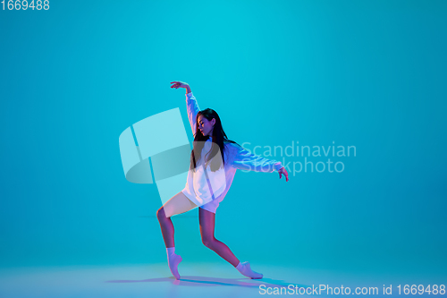 Image of Young and graceful ballet dancer isolated on blue studio background in neon light. Art, motion, action, flexibility, inspiration concept.