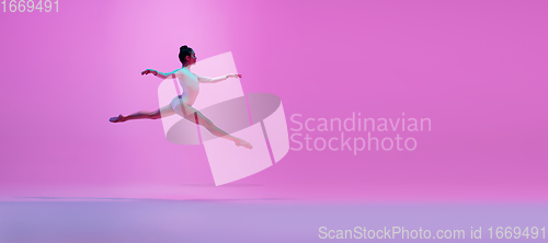 Image of Young and graceful ballet dancer isolated on pink studio background in neon light. Art, motion, action, flexibility, inspiration concept.