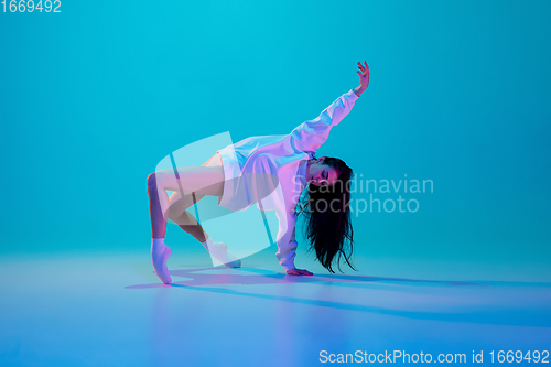 Image of Young and graceful ballet dancer isolated on blue studio background in neon light. Art, motion, action, flexibility, inspiration concept.