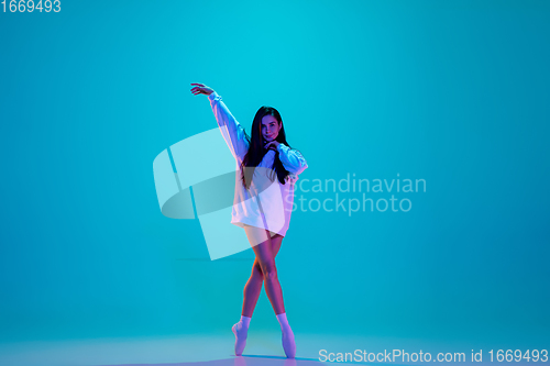 Image of Young and graceful ballet dancer isolated on blue studio background in neon light. Art, motion, action, flexibility, inspiration concept.