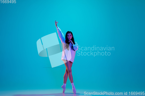 Image of Young and graceful ballet dancer isolated on blue studio background in neon light. Art, motion, action, flexibility, inspiration concept.