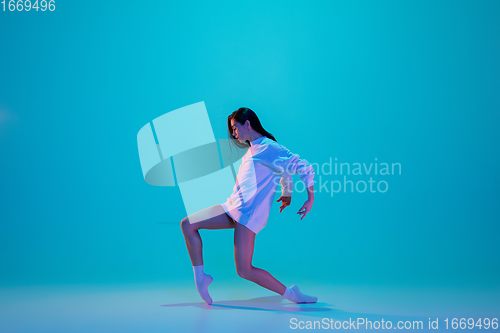 Image of Young and graceful ballet dancer isolated on blue studio background in neon light. Art, motion, action, flexibility, inspiration concept.