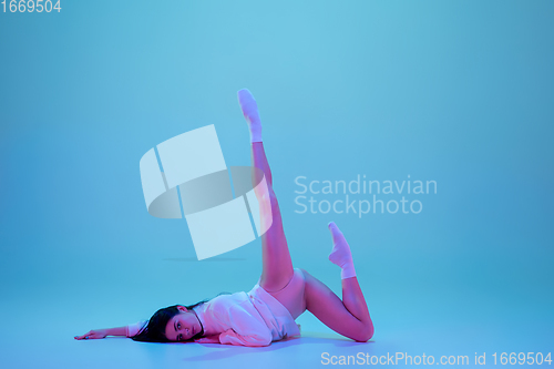 Image of Young and graceful ballet dancer isolated on blue studio background in neon light. Art, motion, action, flexibility, inspiration concept.