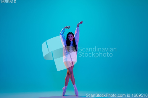 Image of Young and graceful ballet dancer isolated on blue studio background in neon light. Art, motion, action, flexibility, inspiration concept.