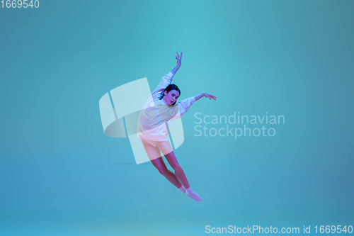 Image of Young and graceful ballet dancer isolated on blue studio background in neon light. Art, motion, action, flexibility, inspiration concept.