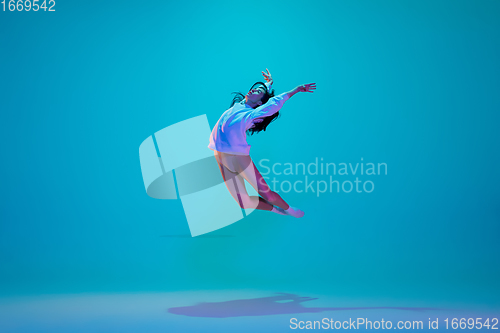 Image of Young and graceful ballet dancer isolated on blue studio background in neon light. Art, motion, action, flexibility, inspiration concept.
