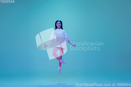 Image of Young and graceful ballet dancer isolated on blue studio background in neon light. Art, motion, action, flexibility, inspiration concept.